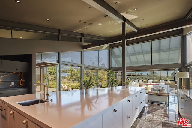 interior space with white cabinets, sink, and a kitchen island with sink