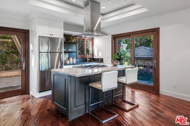 kitchen with island exhaust hood, stainless steel fridge, light stone countertops, dark wood-type flooring, and white cabinetry