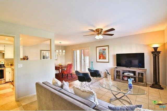 tiled living room with ceiling fan with notable chandelier