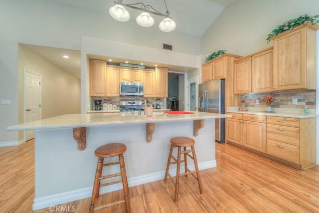 kitchen with appliances with stainless steel finishes, light brown cabinets, tasteful backsplash, and hanging light fixtures