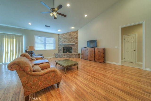 living room featuring light wood-type flooring, high vaulted ceiling, ceiling fan, and a stone fireplace