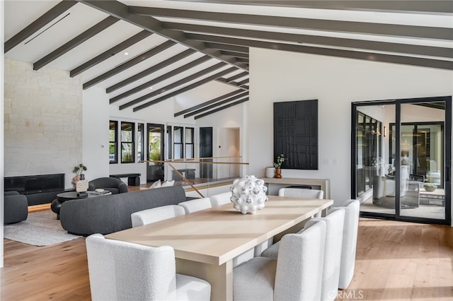 dining space with beamed ceiling, light hardwood / wood-style floors, a stone fireplace, and high vaulted ceiling