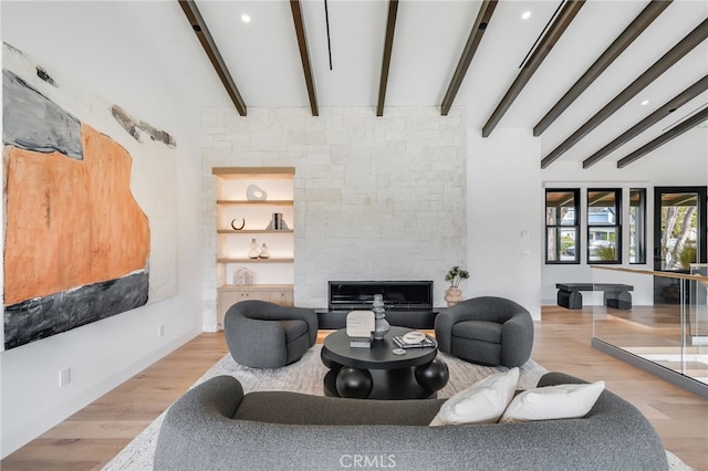 living room featuring beamed ceiling, wood-type flooring, and a stone fireplace