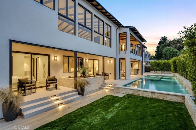 back house at dusk with a lawn, a balcony, and a patio