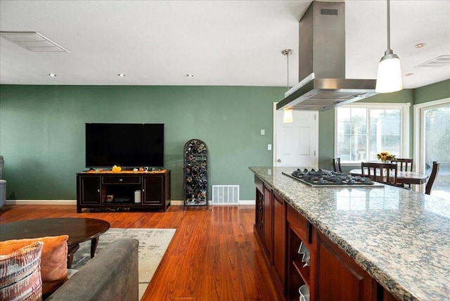 kitchen with dark hardwood / wood-style floors, stainless steel gas stovetop, island exhaust hood, hanging light fixtures, and light stone countertops