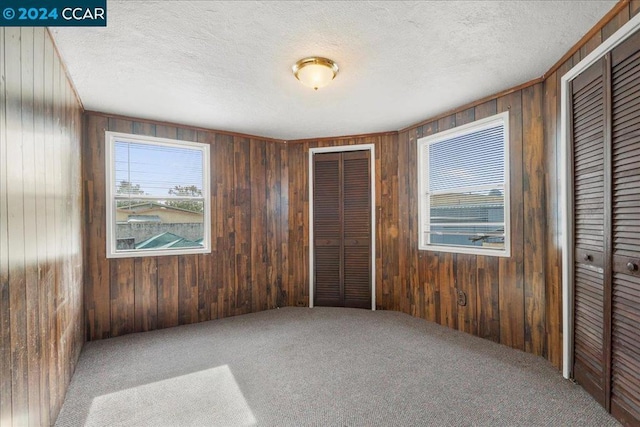 bedroom featuring wood walls, carpet floors, a textured ceiling, and multiple closets