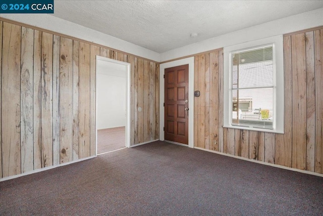 spare room featuring wood walls, dark carpet, and a textured ceiling