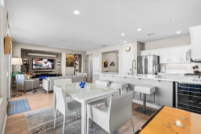 dining space with wine cooler, light hardwood / wood-style flooring, and sink