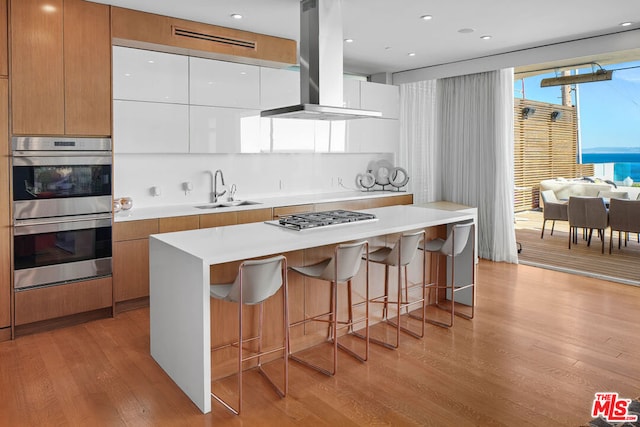 kitchen with white cabinets, sink, light wood-type flooring, appliances with stainless steel finishes, and island range hood