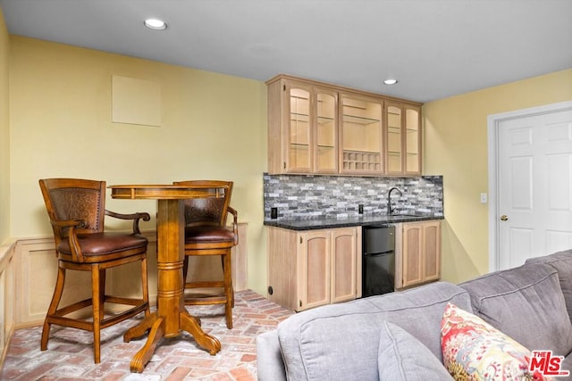 bar featuring light brown cabinetry, backsplash, black fridge, and sink