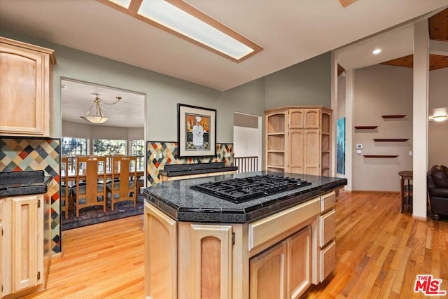 kitchen featuring a center island, light brown cabinets, black gas stovetop, decorative backsplash, and light hardwood / wood-style floors