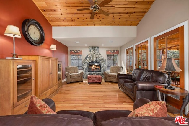 living room featuring ceiling fan, a stone fireplace, light hardwood / wood-style flooring, vaulted ceiling, and wood ceiling