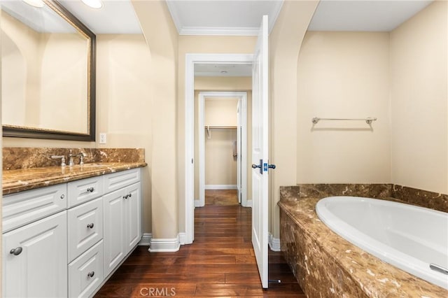 bathroom featuring hardwood / wood-style floors, vanity, ornamental molding, and tiled tub