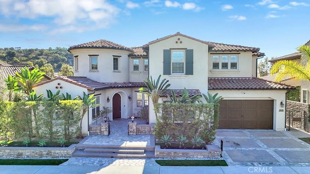 mediterranean / spanish-style house with a garage, driveway, a tiled roof, and stucco siding