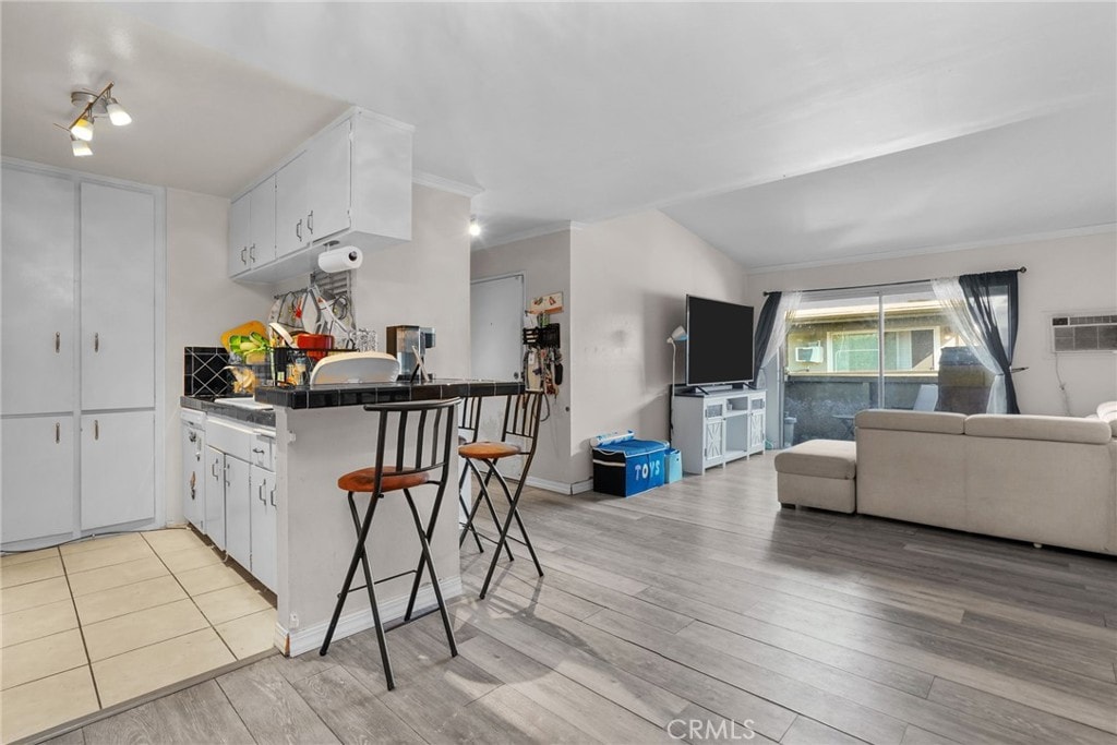 kitchen with a breakfast bar, white cabinets, light wood-type flooring, ornamental molding, and kitchen peninsula