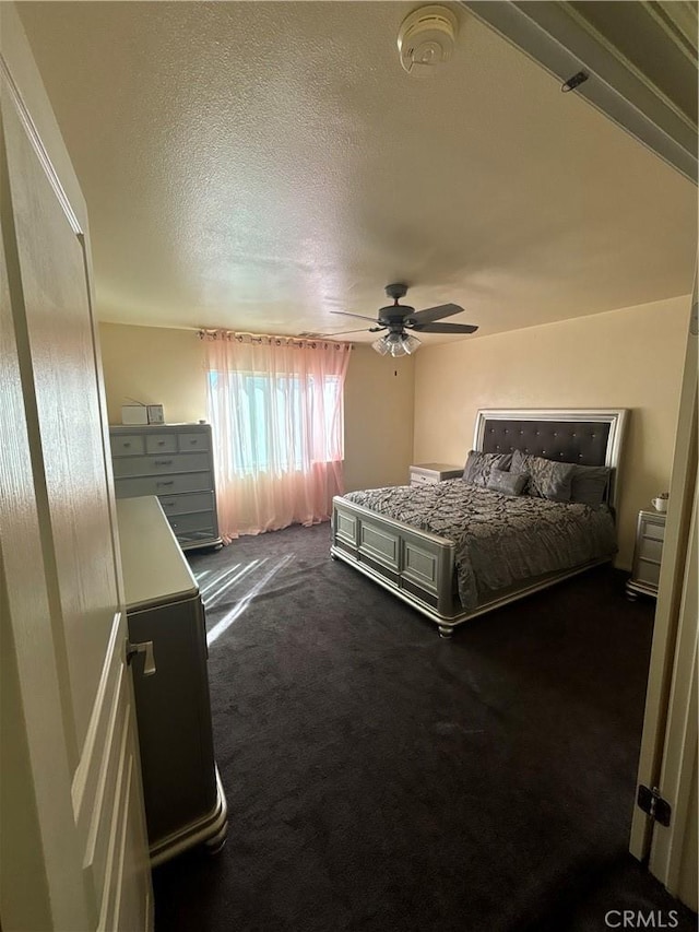 bedroom with ceiling fan, dark carpet, and a textured ceiling