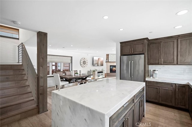 kitchen featuring backsplash, a center island, light hardwood / wood-style floors, stainless steel refrigerator, and a stone fireplace