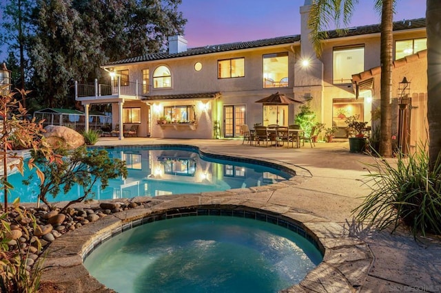 back house at dusk with a pool with hot tub, a balcony, and a patio