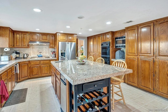 kitchen with a breakfast bar area, a center island with sink, light tile patterned floors, and appliances with stainless steel finishes