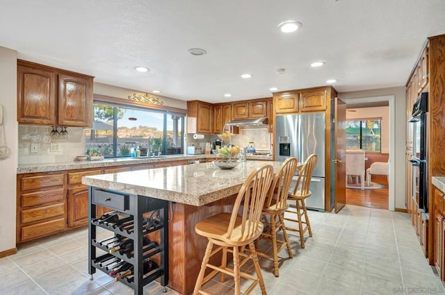 kitchen featuring a kitchen bar, stainless steel refrigerator with ice dispenser, backsplash, double oven, and a kitchen island