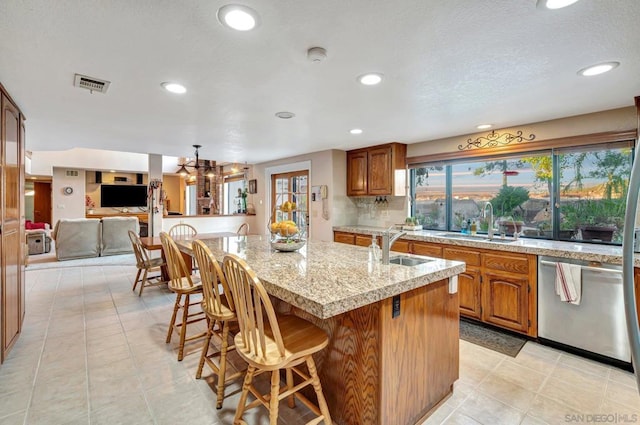 kitchen featuring dishwasher, a center island with sink, a kitchen breakfast bar, hanging light fixtures, and light tile patterned floors