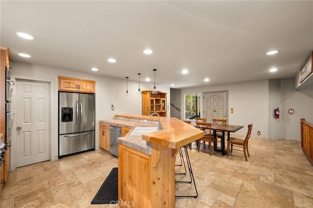 kitchen with a breakfast bar, sink, an island with sink, appliances with stainless steel finishes, and decorative light fixtures