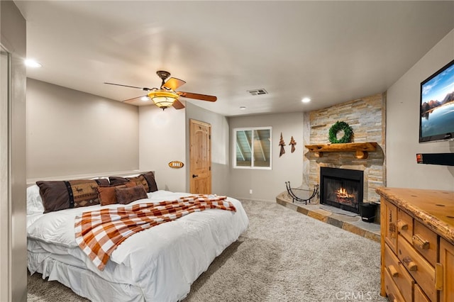 carpeted bedroom featuring ceiling fan and a stone fireplace