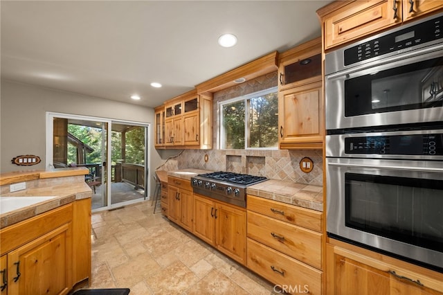 kitchen with tile counters, plenty of natural light, backsplash, and appliances with stainless steel finishes