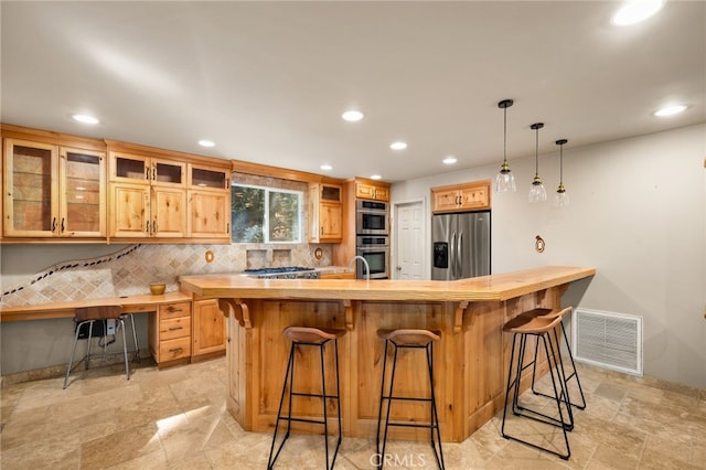 kitchen featuring light brown cabinets, a kitchen island with sink, a kitchen breakfast bar, appliances with stainless steel finishes, and tasteful backsplash