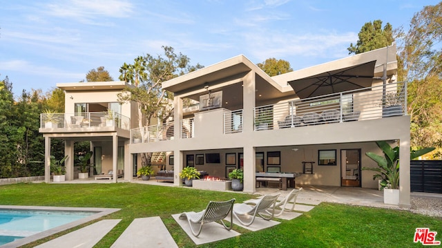 rear view of property featuring a balcony, a yard, and a patio