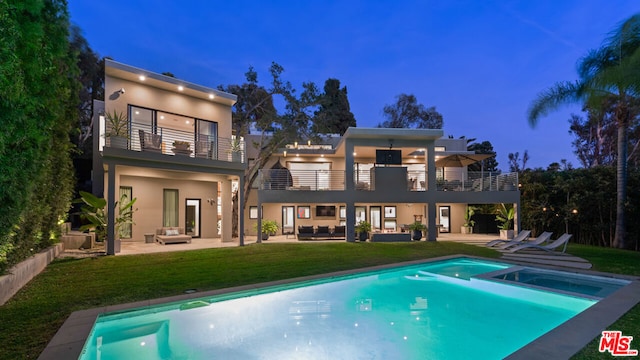 back house at dusk featuring outdoor lounge area, a balcony, a patio area, and a pool with hot tub