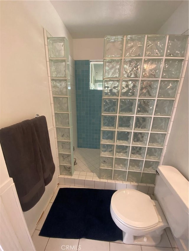 bathroom with toilet, a tile shower, and tile patterned floors