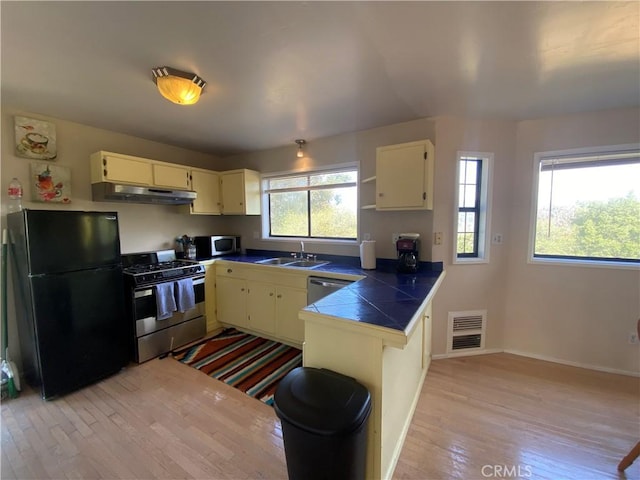 kitchen with cream cabinets, sink, stainless steel appliances, and light wood-type flooring