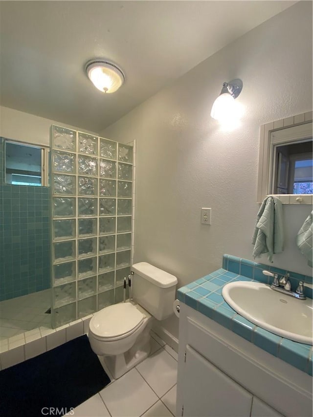 bathroom with tile patterned flooring, toilet, a tile shower, and vanity