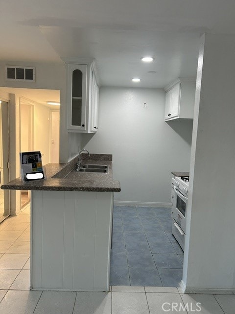 kitchen with white range with gas stovetop, kitchen peninsula, sink, a kitchen bar, and white cabinetry