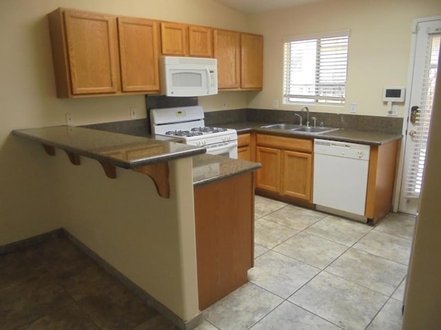 kitchen featuring kitchen peninsula, white appliances, sink, light tile patterned floors, and a breakfast bar area