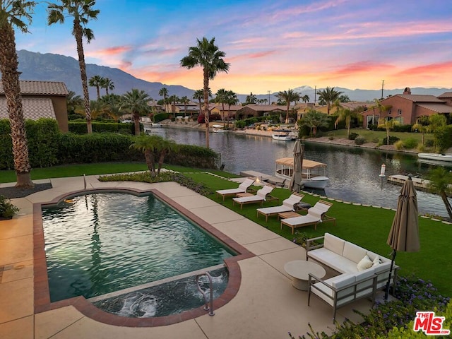 pool at dusk featuring an outdoor living space, a patio, a water and mountain view, and a lawn