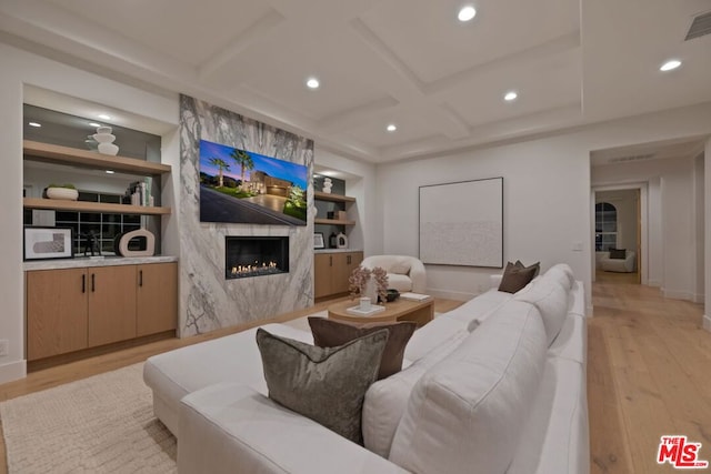 living room featuring a high end fireplace, beam ceiling, light hardwood / wood-style flooring, and coffered ceiling