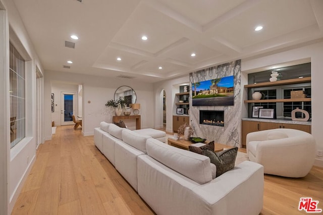 living room with beamed ceiling, a high end fireplace, coffered ceiling, and light wood-type flooring