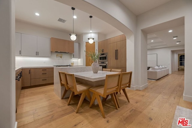 kitchen with pendant lighting, a center island, white cabinets, light hardwood / wood-style flooring, and tasteful backsplash