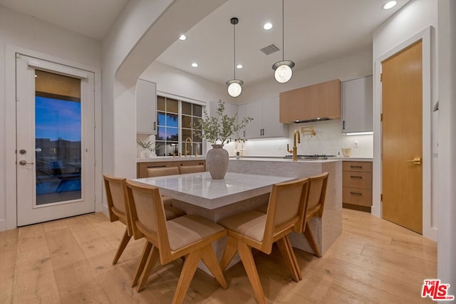 kitchen with decorative backsplash, a kitchen island with sink, light hardwood / wood-style floors, white cabinetry, and hanging light fixtures