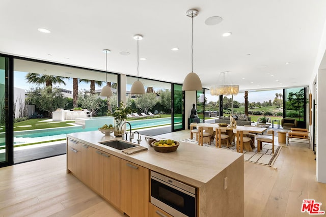 kitchen with a wealth of natural light, light hardwood / wood-style floors, stainless steel microwave, and an island with sink