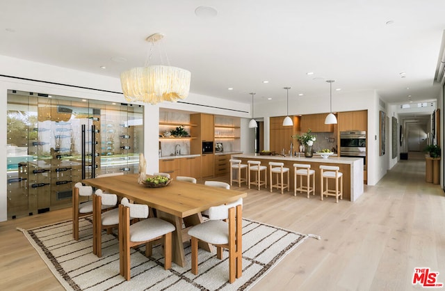 dining space with built in shelves, sink, light hardwood / wood-style flooring, and an inviting chandelier