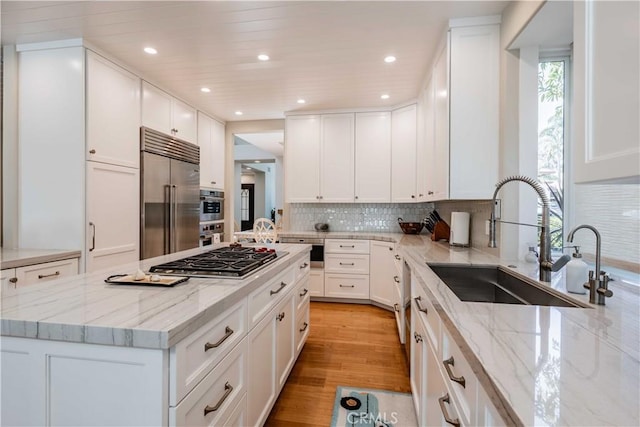 kitchen with light stone countertops, appliances with stainless steel finishes, sink, light hardwood / wood-style flooring, and white cabinetry