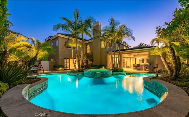 pool at dusk featuring a patio area, an outdoor bar, and an in ground hot tub