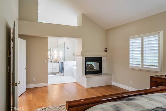 unfurnished bedroom with a multi sided fireplace, high vaulted ceiling, and light wood-type flooring