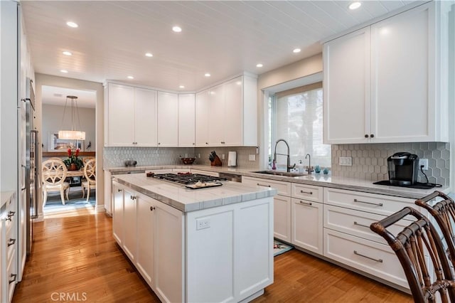 kitchen with light wood-type flooring, a kitchen island, stainless steel gas cooktop, sink, and white cabinetry