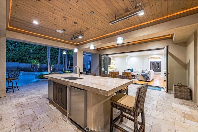 kitchen featuring sink, an island with sink, a tray ceiling, butcher block counters, and wood ceiling