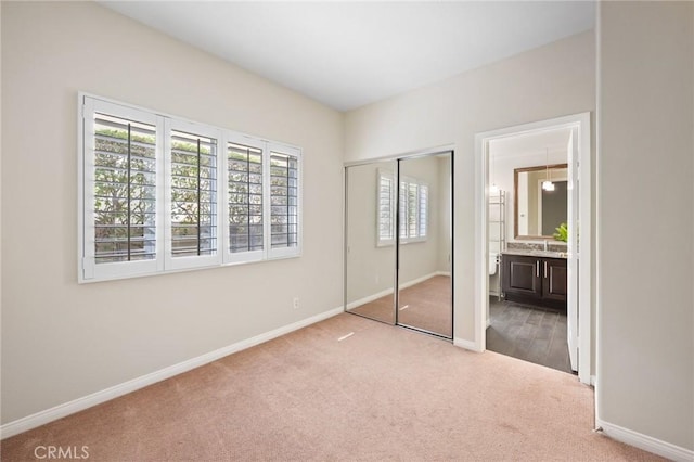 unfurnished bedroom with light colored carpet, a closet, and ensuite bathroom