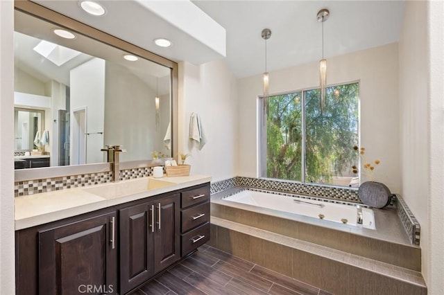 bathroom featuring radiator heating unit, vaulted ceiling with skylight, tiled bath, backsplash, and vanity